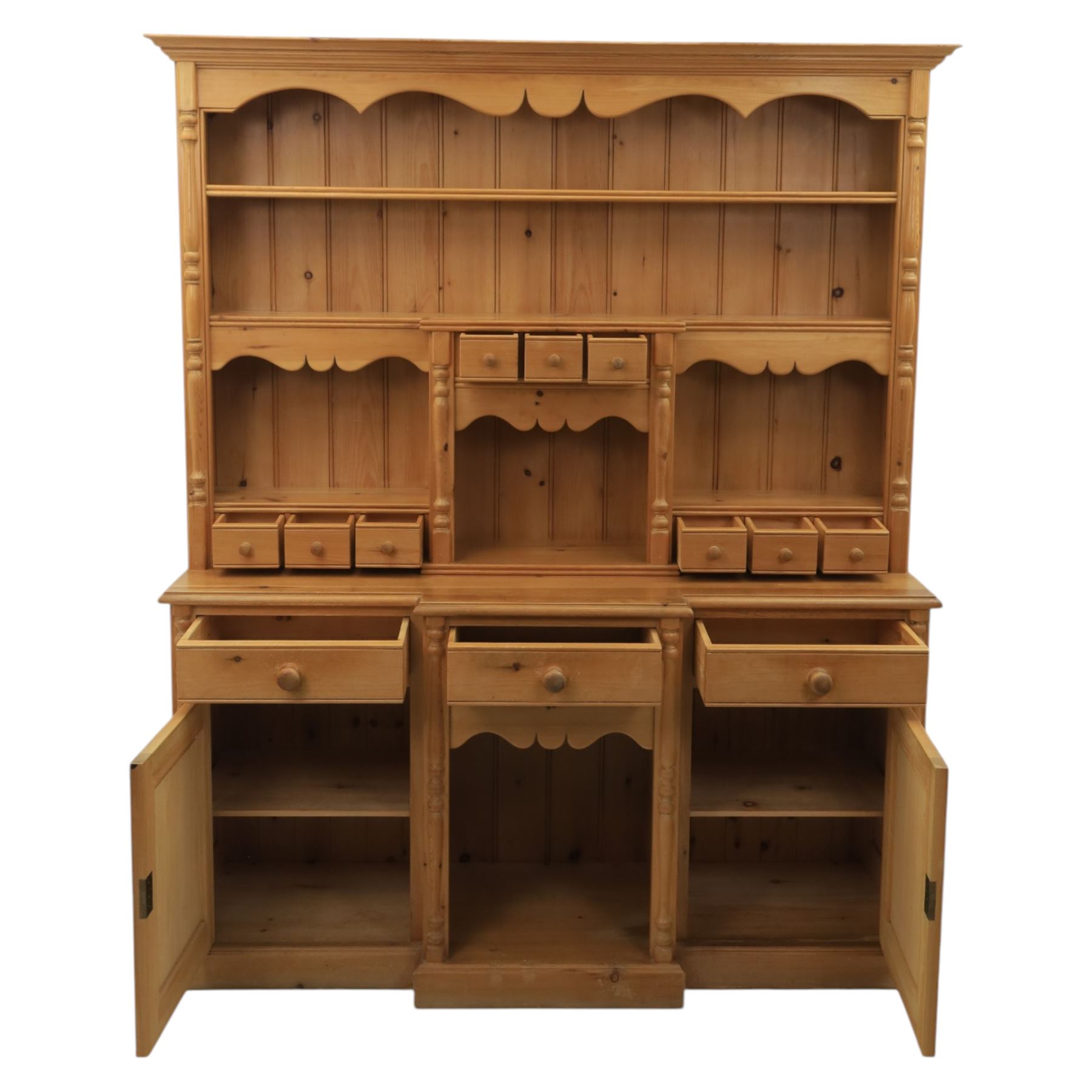 20th century country style waxed pine housekeeper’s cupboard, upper section with moulded cornice, shaped aprons and open shelving around central drawer arrangement, the lower section fitted with three drawers and two cupboards with panelled doors, raised on a plinth base
