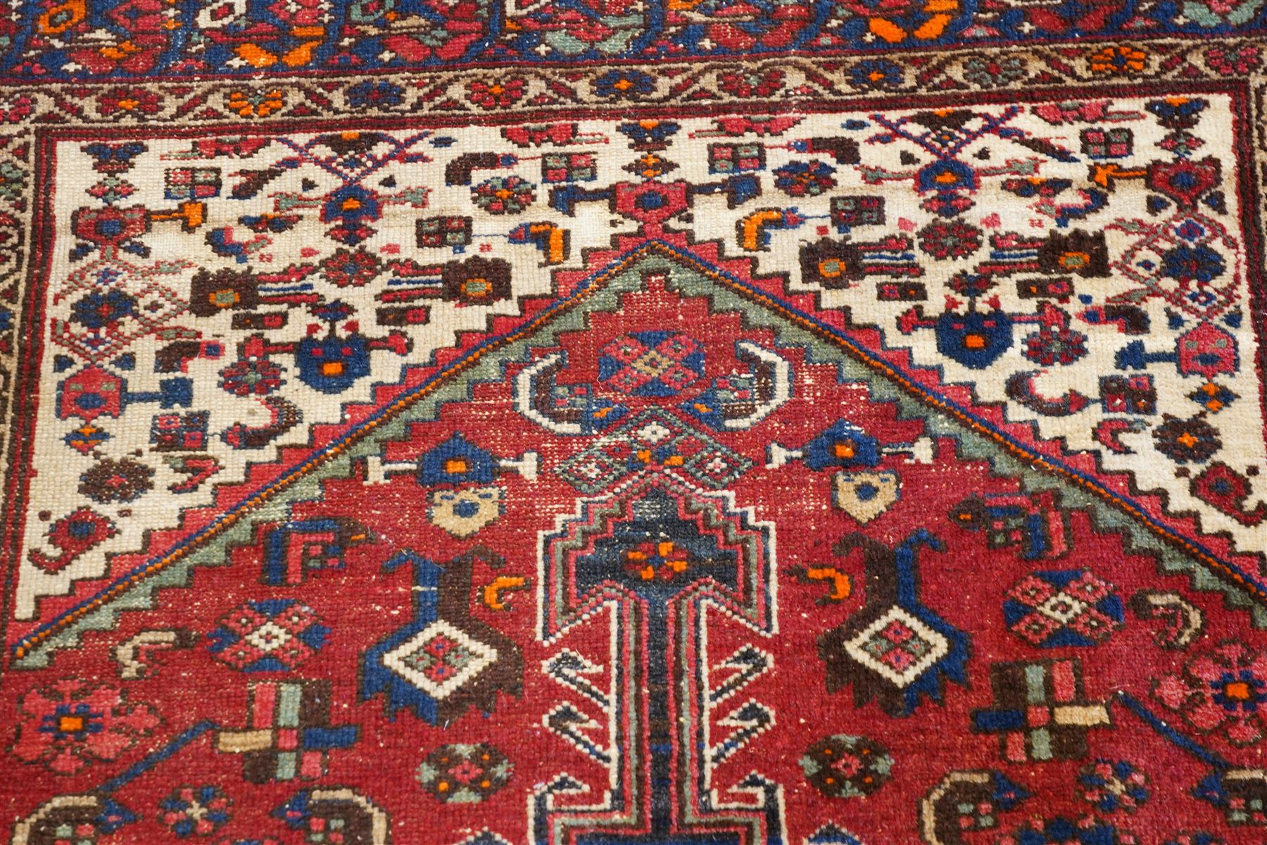 Persian Heriz crimson ground carpet, the central navy geometric medallion on a red crimson ground field, surrounded by further geometric stylised motifs and foliate designs, enclosed by multiple guard-lines  