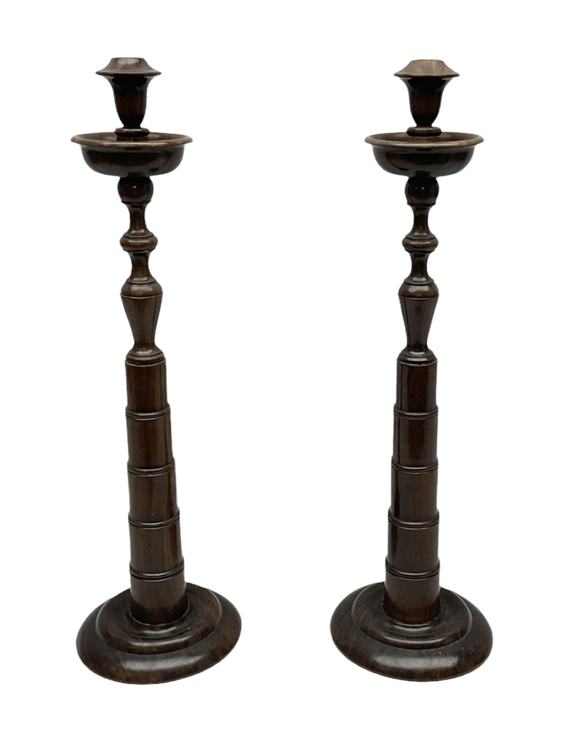 Pair of turned wooden candlesticks, the central column of stepped form raised upon circular spreading base, with drip trays, H56cm