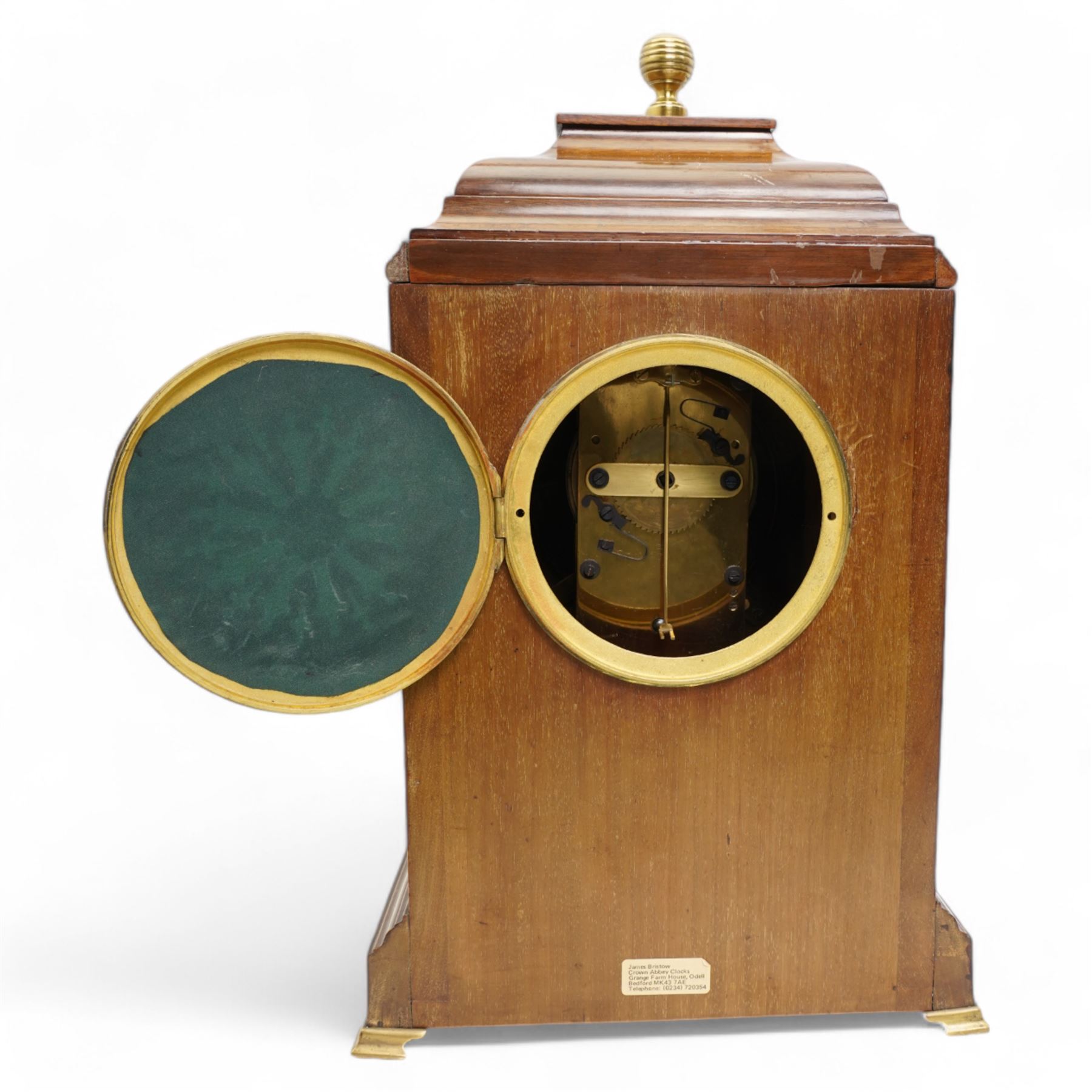 Edwardian- Early 20th century 8-day mahogany mantle clock, with a stepped pediment and brass finial, recessed brass pilasters and brass inlay to the front with a conforming plinth raised on bracket feet, silvered dial with Arabic numerals and steel spade hands within a glazed brass bezel, single train timepiece movement with pendulum and key.
