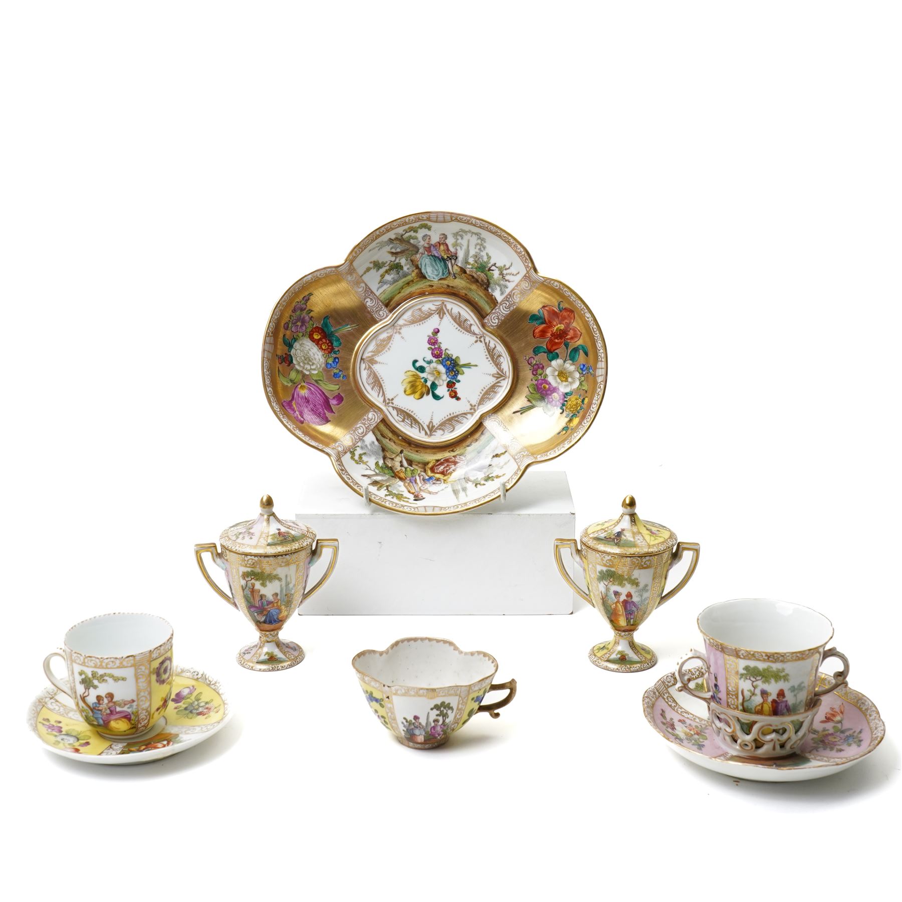 Collection of Helena Wolfsohn Dresden porcelain works, comprising a quatrefoil dish, D24cm, a chocolate cup with socketed saucer, two teacups, one with saucer, and a pair of twin-handled covered cups, each decorated with panels of flowers and courting scenes, various blue marks to bases