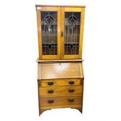 Early 20th century Arts and Crafts oak bureau bookcase, twin leaded and glazed stained glass doors enclosing two shelves, over bureau section with fall-front inlaid with sunburst motif, fitted interior of pigeonholes and shelves, on bracket feet