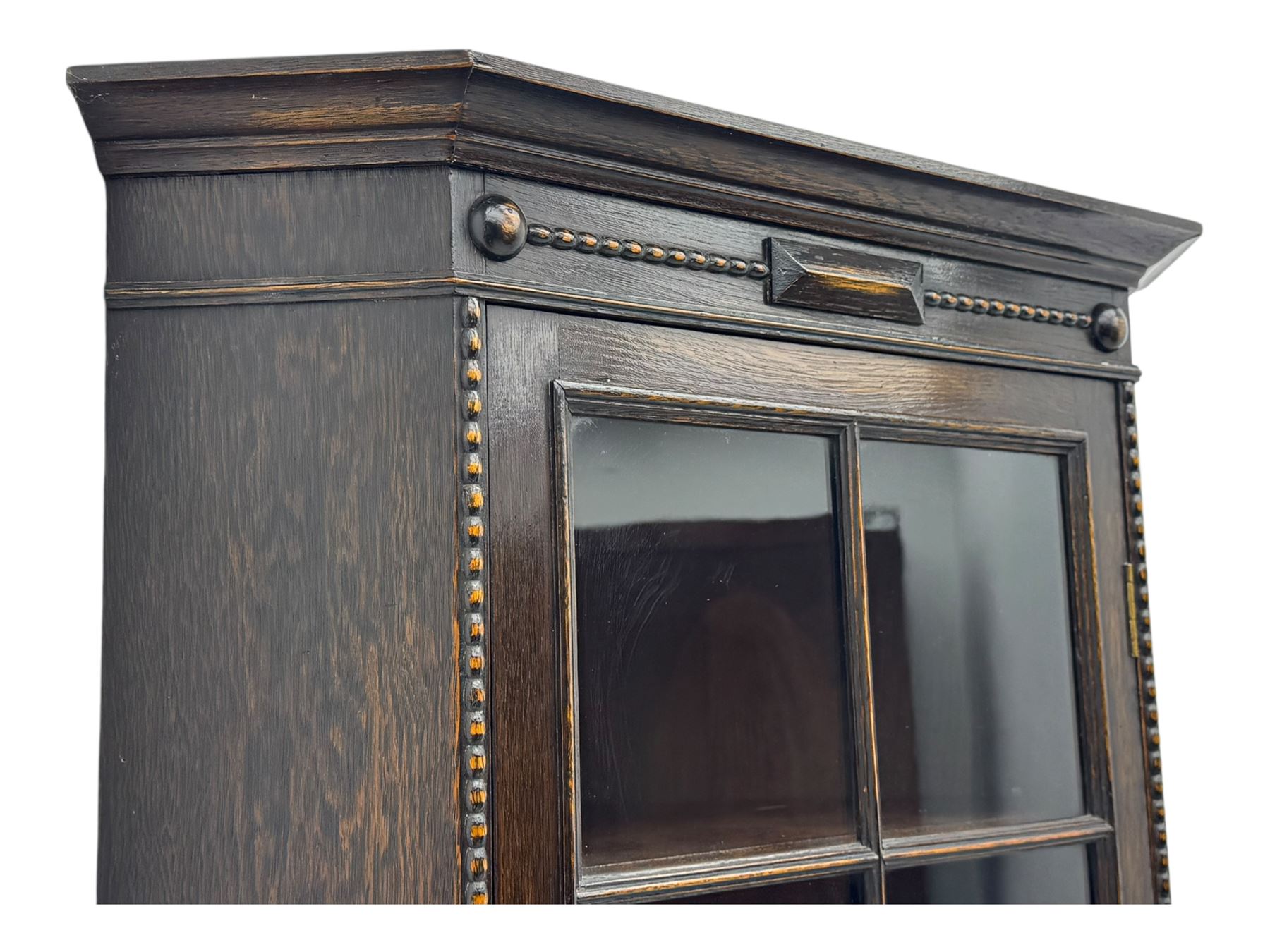 Early 20th century oak corner display cabinet, the moulded canted cornice over a single glazed door with geometric astragal bars, shelved interior, the lower tier forming a triangular platform, raised on four barley-twist supports united by shaped brackets