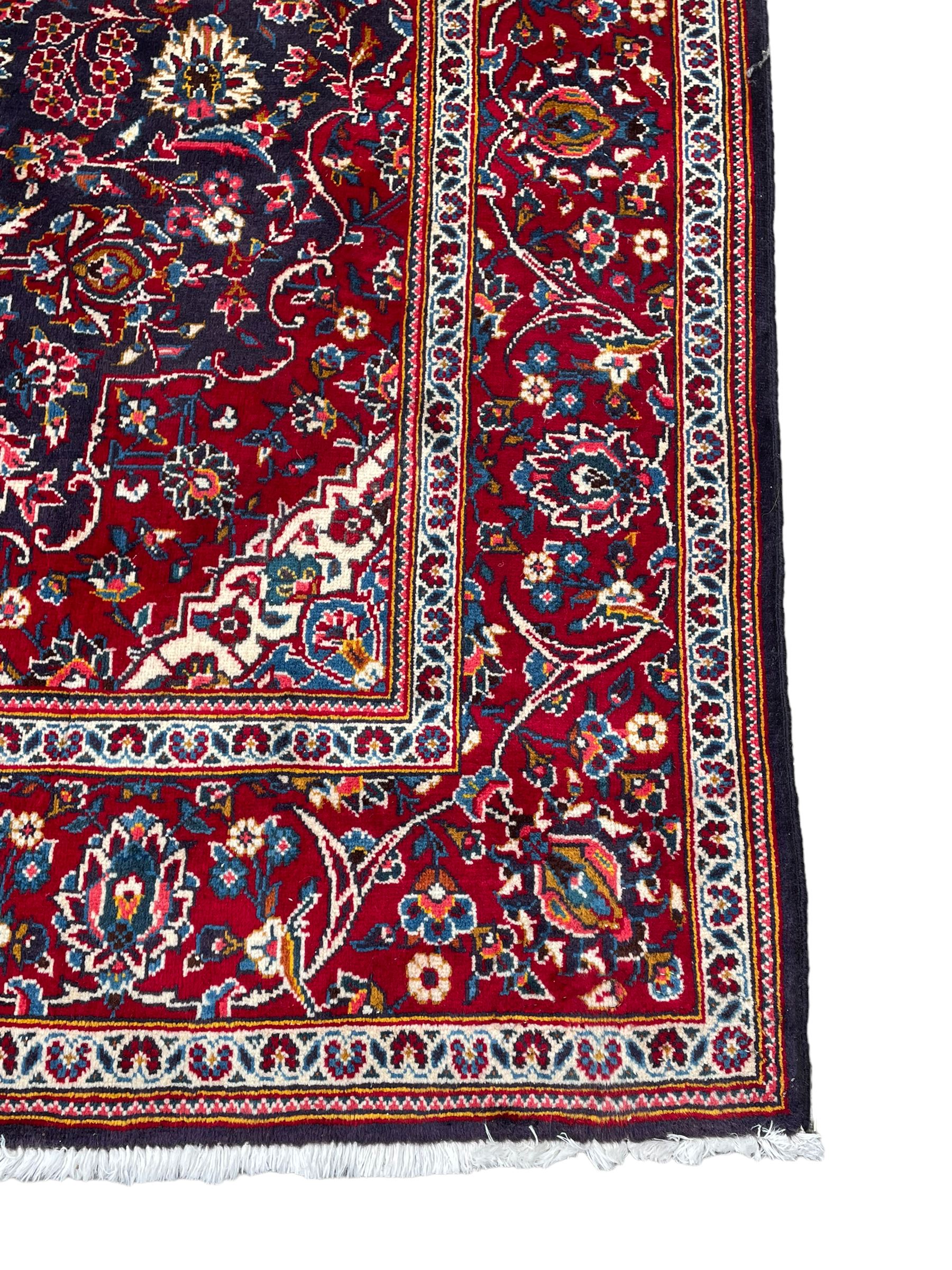 Persian indigo ground rug, the central crimson pole lozenge medallion surrounded by interlacing floral patterns, the main border with repeating plant motifs connected by scrolling branches