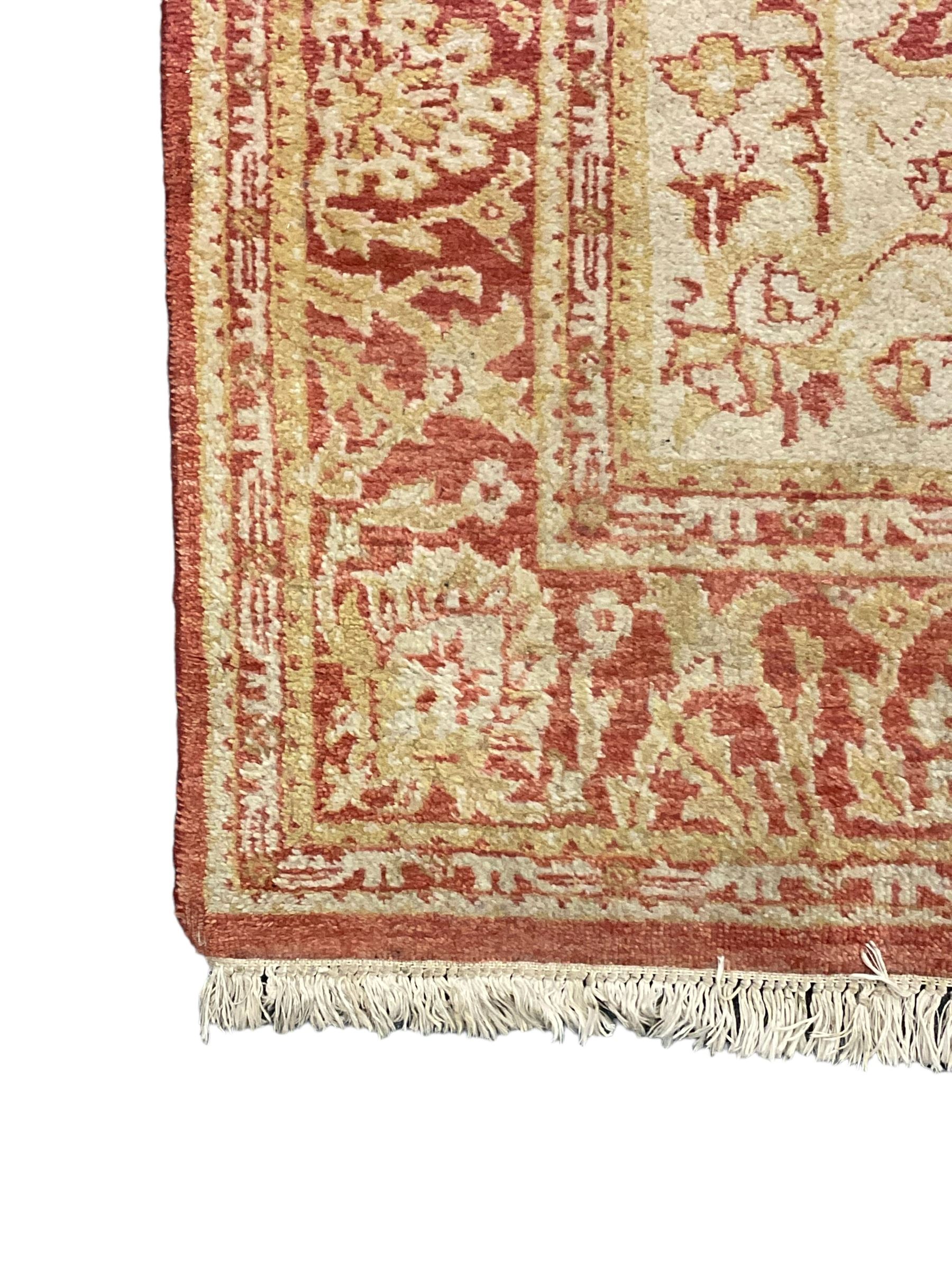 Persian design beige and crimson ground rug, the field decorated with interlacing scrolled foliage, repeating border within guard stripes 