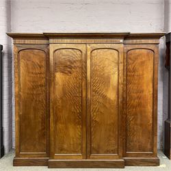 19th century figured mahogany quadruple breakfront press wardrobe, projecting cornice with banded frieze over arch panelled doors, the interior fitted with three sliding trays over two short and three long graduating drawers with recessed brass handles, flanked by two hanging cupboards with hooks