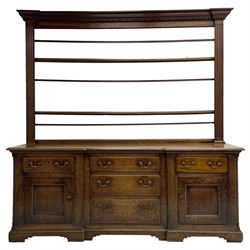 George III oak dresser, projecting dentil cornice over three heights plate rack enclosed by fluted uprights, the dresser fitted with five drawers and two panelled cupboards, canted corners with fluted quarter columns, on bracket feet