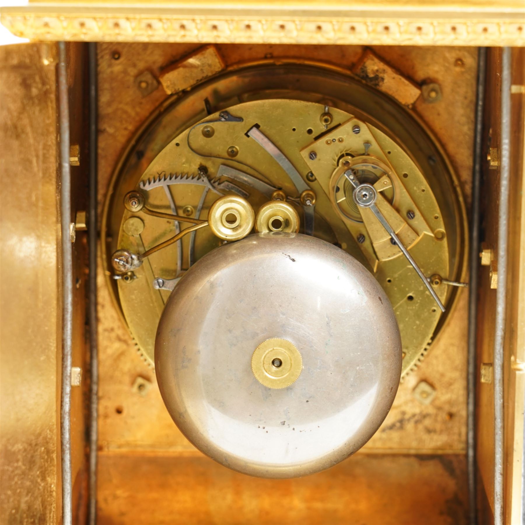 Fine Swiss ormolu 8-day early 19th century Pendule d'Officer style clock c1820,  circular double train ting-tang movement striking the quarters on a graduated pair of bells and sounding the hour on one, going train with a vertical platform lever escapement and over sprung balance, rack striking, with visible hour and quarter strike work to the backplate, movement unsigned, convex enamel dial with Roman numerals and steel moon hands behind a glazed gilt bezel, case with a scroll cast handle to the arched top with applied rococo decoration to the tympanum, both sides of the case adorned with a military trophy of arms motif and deep frieze with foliate arcading beneath, on a rectangular plinth with decorative scroll engraved bracket feet. With Key.   