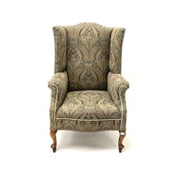 Early 20th century high wing back sprung armchair, upholstered in a stylised patterned fabric and trimming, cabriole supports and castors