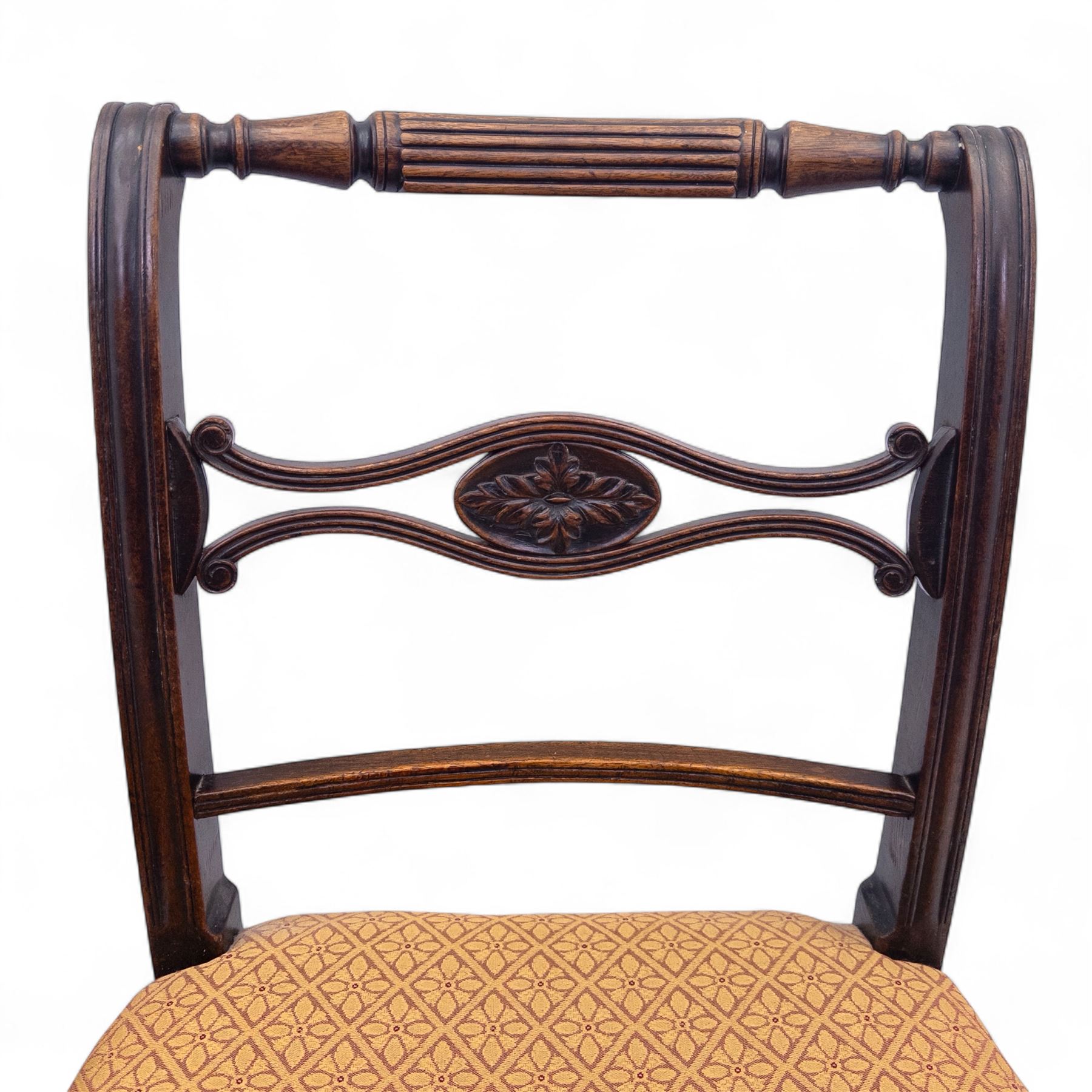 Pair of Regency mahogany side chairs, reeded bar backs centred by oval paterae, overstuffed seats upholstered in gold geometric patterned fabric, on turned tapering front supports 