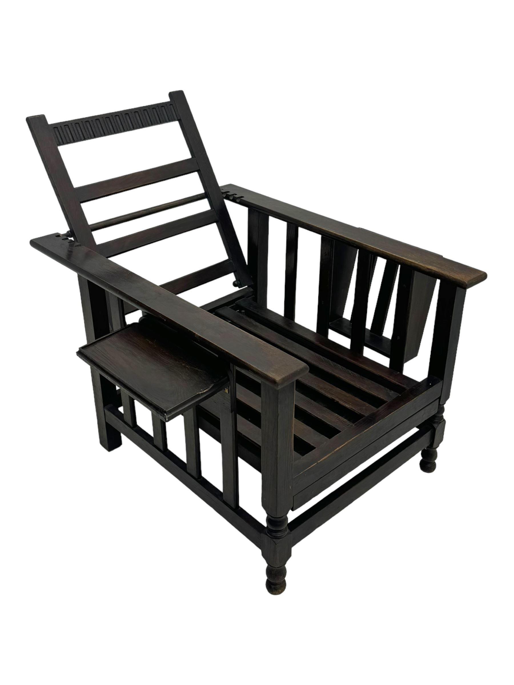 Late Victorian oak steamer chair, adjustable slatted backrest with grooved crest rail, wide armrests extending to a sliding adjustable footrest, open frame sides with vertical slats, side magazine rack and collapsible table, raised on turned front supports