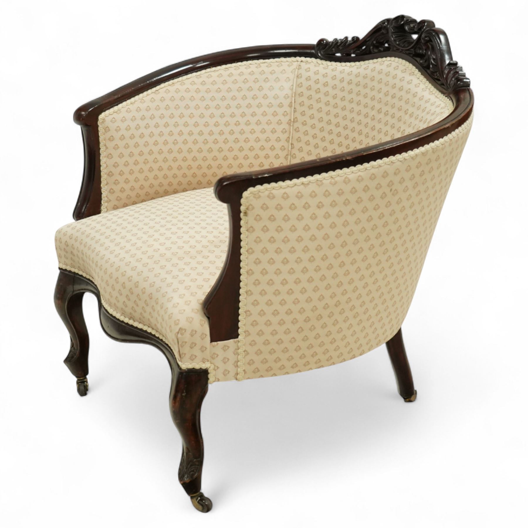 Victorian carved mahogany tub chair, upholstered in cream patterned fabric, with pierced foliate carved top rail, curved back and seat, serpentine seat rail, on cabriole front legs with brass castors