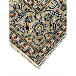 Persian Kashan ivory ground carpet, overall floral design, the field decorated with scrolling and interlaced leafy branches interspersed with palmettes, scrolling border decorated with stylised plant motifs, within floral pattern guard stripes 
