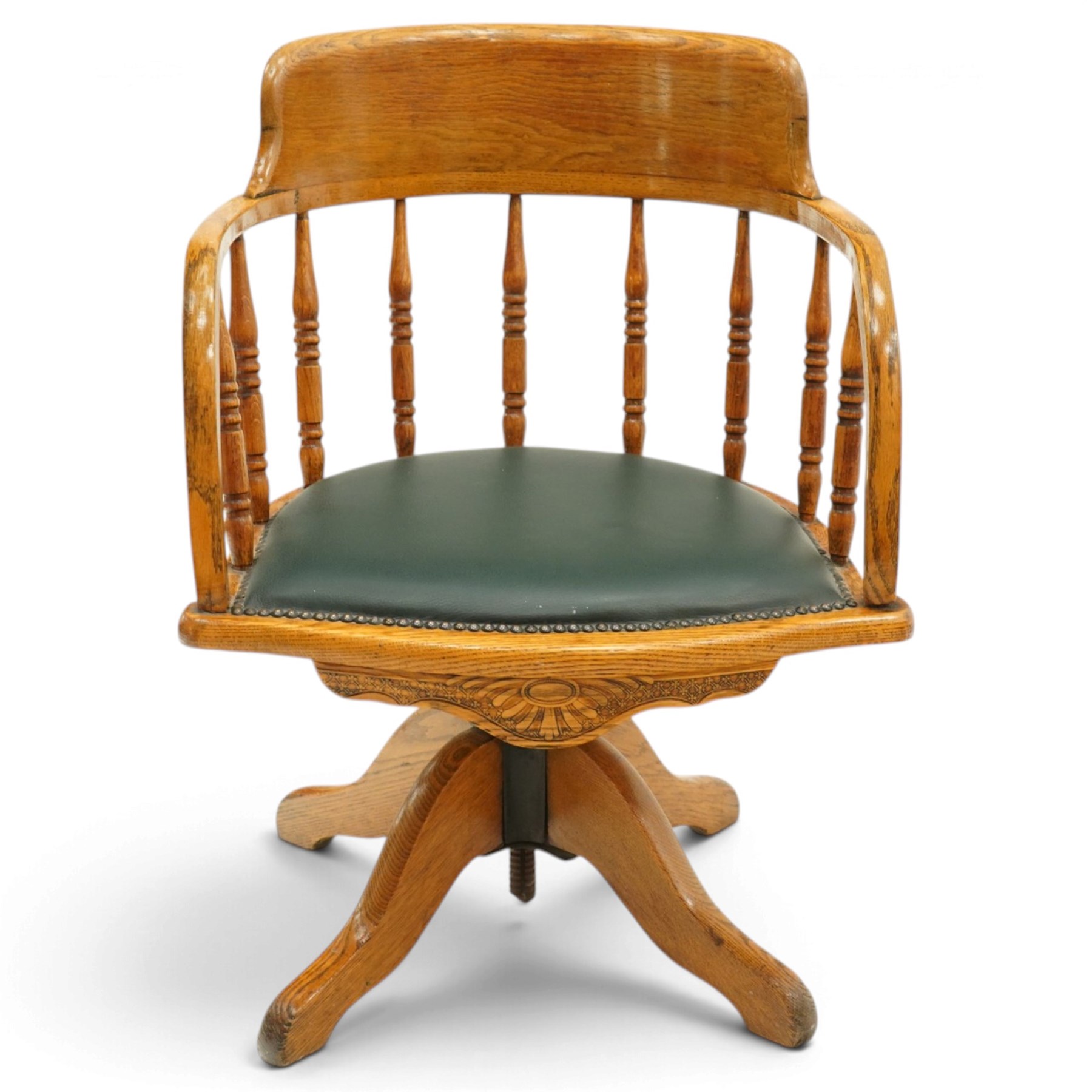 Edwardian oak captains swivel desk chair of tub form, shaped cresting rail over spindle supports and green-leather upholstered seat, foliate apron over swivel action and four-spoke base