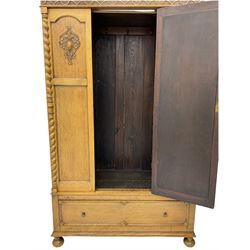 Early 20th century oak wardrobe, projecting cornice of blind fret-work frieze, oval bevel edge mirror door, half spiral turned pilasters, drawer to base with mouldings, on turned bun feet