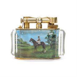 Rare one off special commission Dunhill Sporting Horse Racing half-giant 'Aquarium' table lighter, circa 1955, the lucite panelled body engraved in reverse intaglio technique and hand-painted with Nicholas Nickleby in action, winner of the Royal Hunt Cup, Ascot June 1955, the reverse with jockey Willie Snaith mounted upon Nicholas Nickleby, the gold plated top with arm stamped Dunhill Reg. No 737418, the base stamped DUNHILL LIGHTER, H7.5cm W10cm D5cm

Provenance:
Commissioned by the owner of Nicholas Nickleby, the lighter was gifted to Colin Hetherton, a young veterinary surgeon whose intervention saved Nickleby from certain retirement. Hetherton’s expert care and persistence brought the horse back to full health, culminating in a win that stunned the Ascot crowd.
