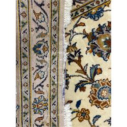 Persian Kashan ivory ground carpet, the field decorated with trailing foliate branches and stylised flower head motifs, guarded border with repeating design decorated with scrolling leafy branch and plant motifs 