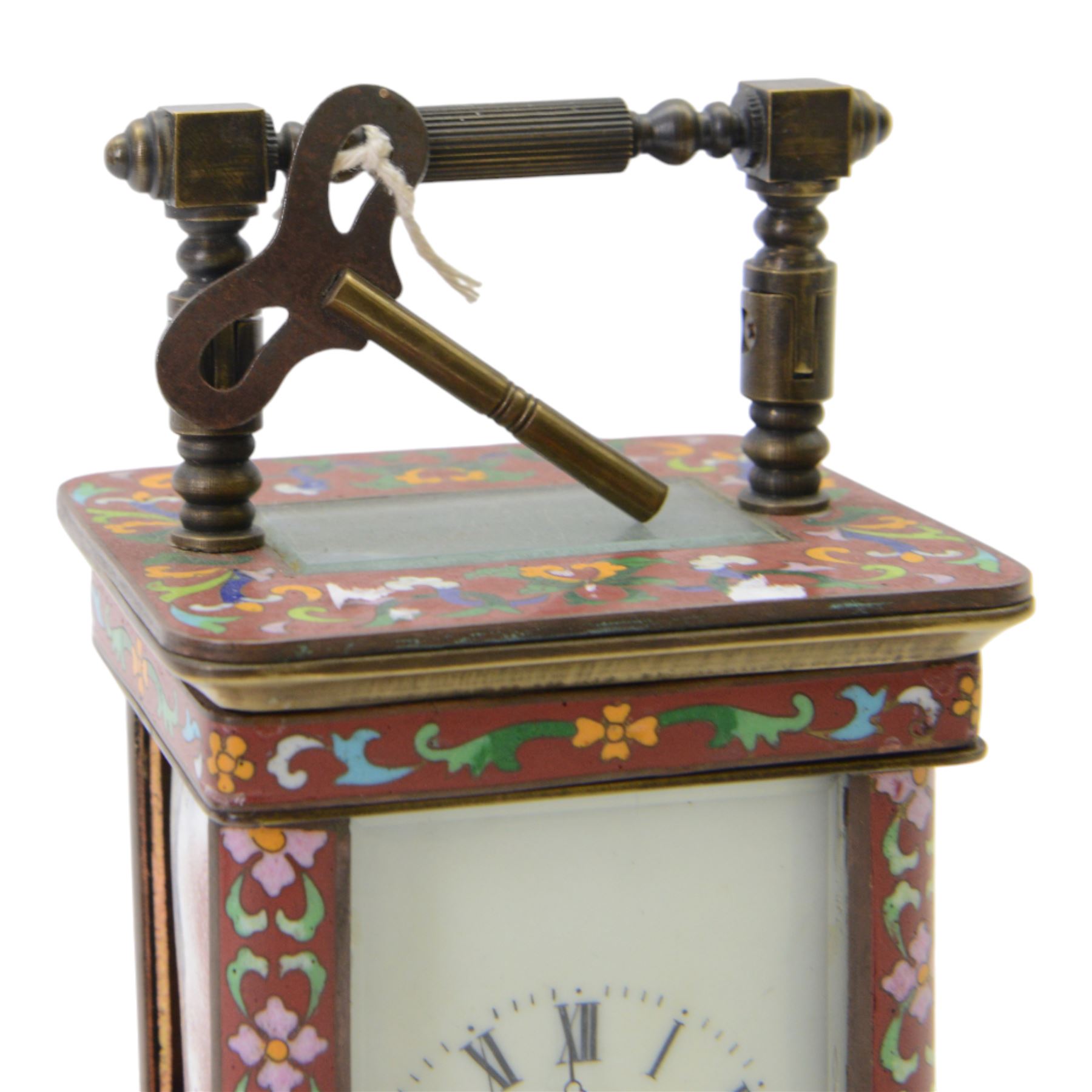 Late 20th century- Chinese 8-day timepiece carriage clock with Cloisonne work on a red ground to the four pillars, base and cornice, with painted porcelain panels to the sides, white enamel dial with Roman numerals and trefoil steel hands, platform escapement wound and set from the rear. With Key.