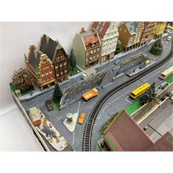 Table top 'N' gauge continental scenic layout as a split level town with various loops of track, station with numerous platforms, engine shed, assorted buildings, roads with motor vehicles and figures, tunnels, trees, river with bridge, tram depot etc 122 x 52cm