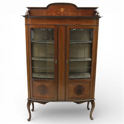 Edwardian mahogany display cabinet, arched back with satinwood and harewood marquetry foliate decoration above a moulded cornice, serpentine front fitted with twin glazed doors with astragal bars, the lower door panels inlaid with oval reserves, standing on elegant cabriole legs terminating in pad feet