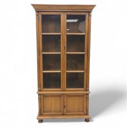 Pair of late 20th century Thai hardwood display cabinets, each with moulded cornice over twin glazed doors enclosing adjustable shelves, panelled cupboard doors below flanked by fluted columns, raised on bun feet