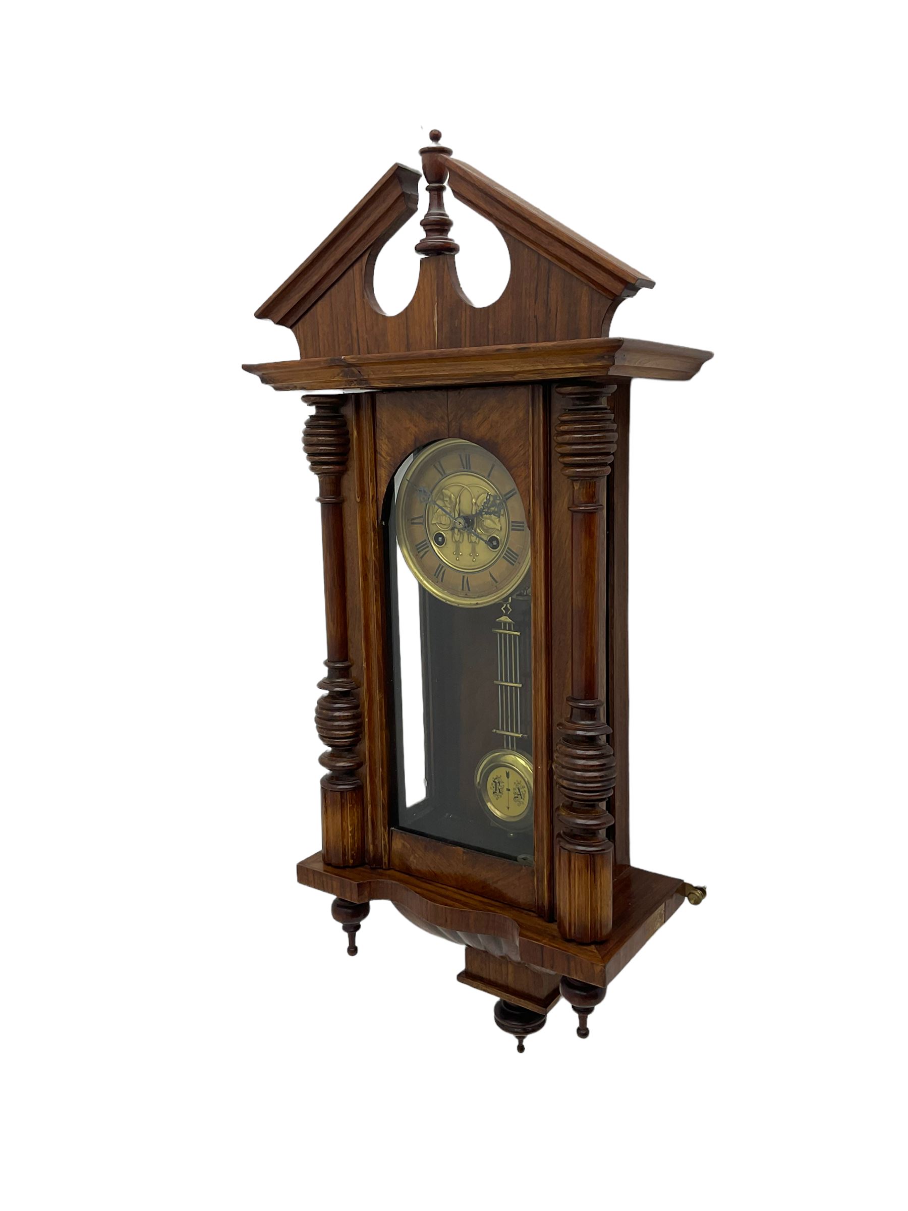 German early 20th century wall clock in a mahogany case with an architectural pediment and turned finial, with applied carving and pendant finials, fully glazed door with a visible gridiron pendulum, eight-day spring driven striking movement striking the hours on a gong, dial with Roman numerals to the chapter and a gilt repoussé centre.   

