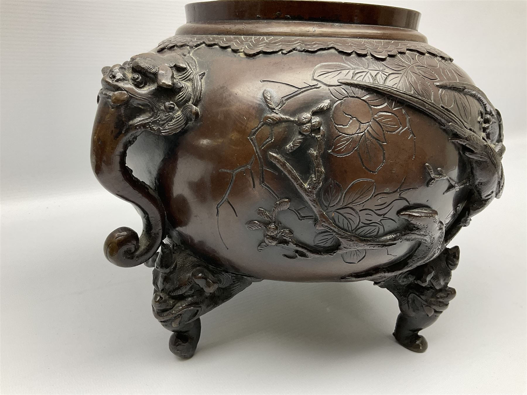 Japanese bronzed koro, the body of globular form with twin cast zoomorphic mask handles, decorated in relief with birds upon blossoming branches, against a ground incised with rushes and peonies, the flat toped domed cover with pierced band and surmounted by a cast figure of a Foo dog, the whole upon three zoomorphic mask feet, with impressed character type mark beneath, H35.5cm