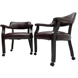 Pair of tub shaped armchairs, upholstered in burgundy faux leather with studwork, raised on square supports with castors