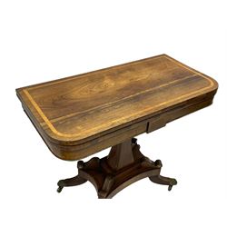 Regency rosewood and brass inlaid card table, the rectangular fold-over and swivelling top with rounded corners with a satinwood band, opening to reveal a blue baize lined interior playing surface, the frieze with a raised panel with satinwood stringing and a lower beaded brass edge, the concave and canted column with a shaped platform base applied with scrolls with brass star inlays and stringing, quadruple splayed supports terminating in foliate cast cups and castors