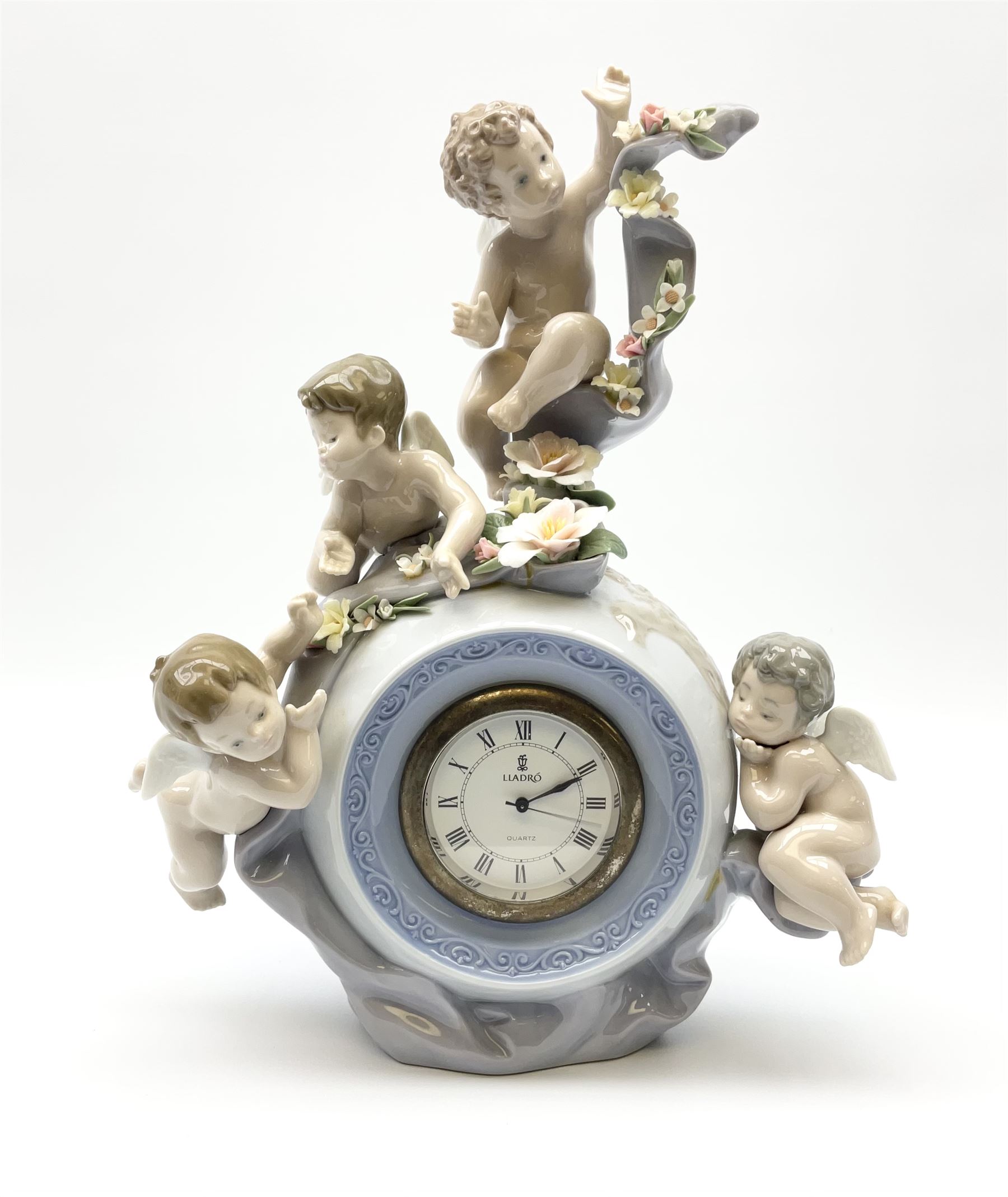 A Lladro mantel clock modelled as a globe with inset clock, surmounted by four putti and floral garlands, with blue printed mark and impressed 5973 beneath, H29cm.