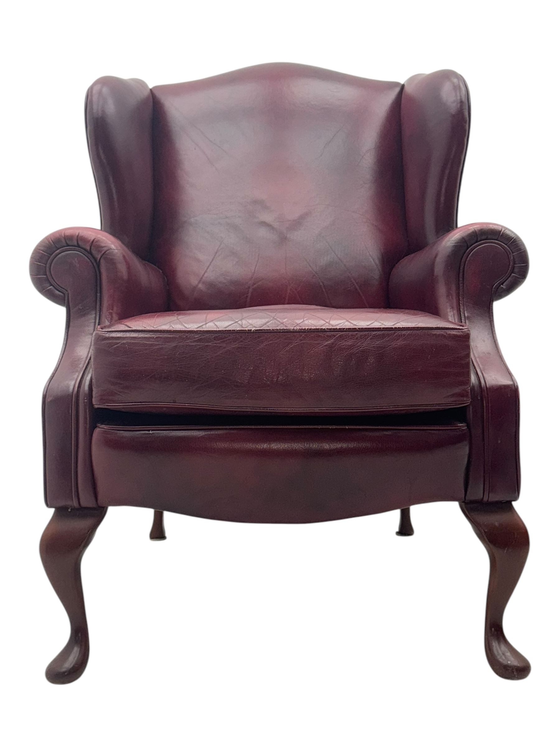 Mid-20th century leather wingback armchair, upholstered in deep burgundy leather, featuring a shaped backrest and scrolled armrests, raised on mahogany cabriole front supports