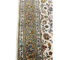 Persian Kashan ivory ground carpet, the field decorated with trailing foliate branches and stylised flower head motifs, guarded border with repeating design decorated with scrolling leafy branch and plant motifs 