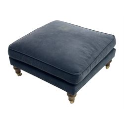 Contemporary square footstool upholstered in navy armour smart velvet, featuring a deep padded top, turned wood supports, and brass castors