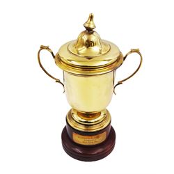 Edwardian silver-gilt twin handled trophy cup and cover, with two curved handles, the domed cover with urn finial, upon domed stepped foot and cylindrical mahogany base with applied plaque, hallmarked Skinner & Co, London 1908, total H29.7cm