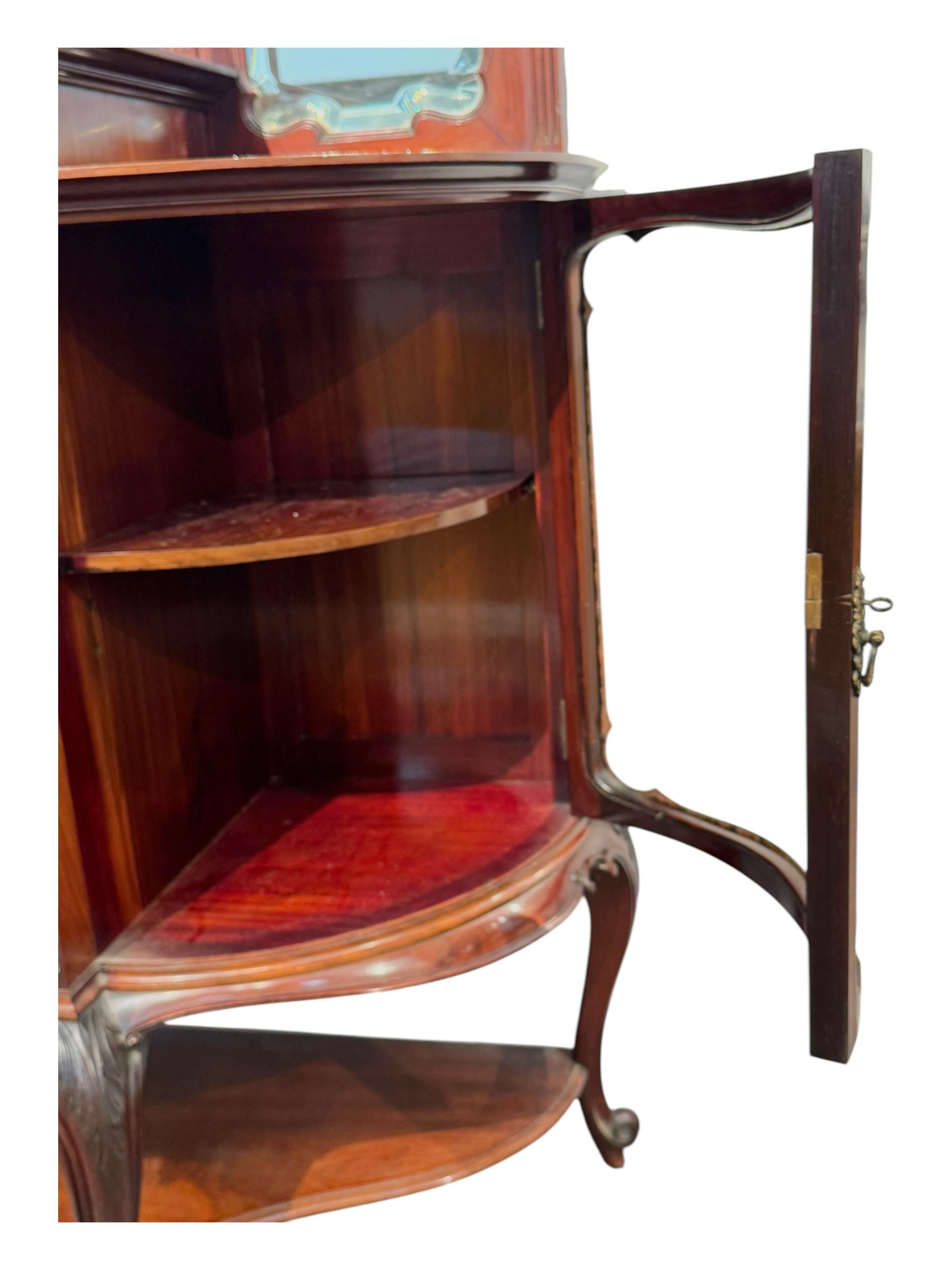 Late 19th century mahogany mirror back cabinet, shaped C-scroll pediment decorated with carved acanthus leaf cartouche and shells, shaped canopy top with applied foliate carvings over triple bevelled mirror back, central cupboard enclosed by panelled door carved with musical instruments, scrolls and shells, flanked by two glazed cabinets, on acanthus leaf carved cabriole supports united by undertier 