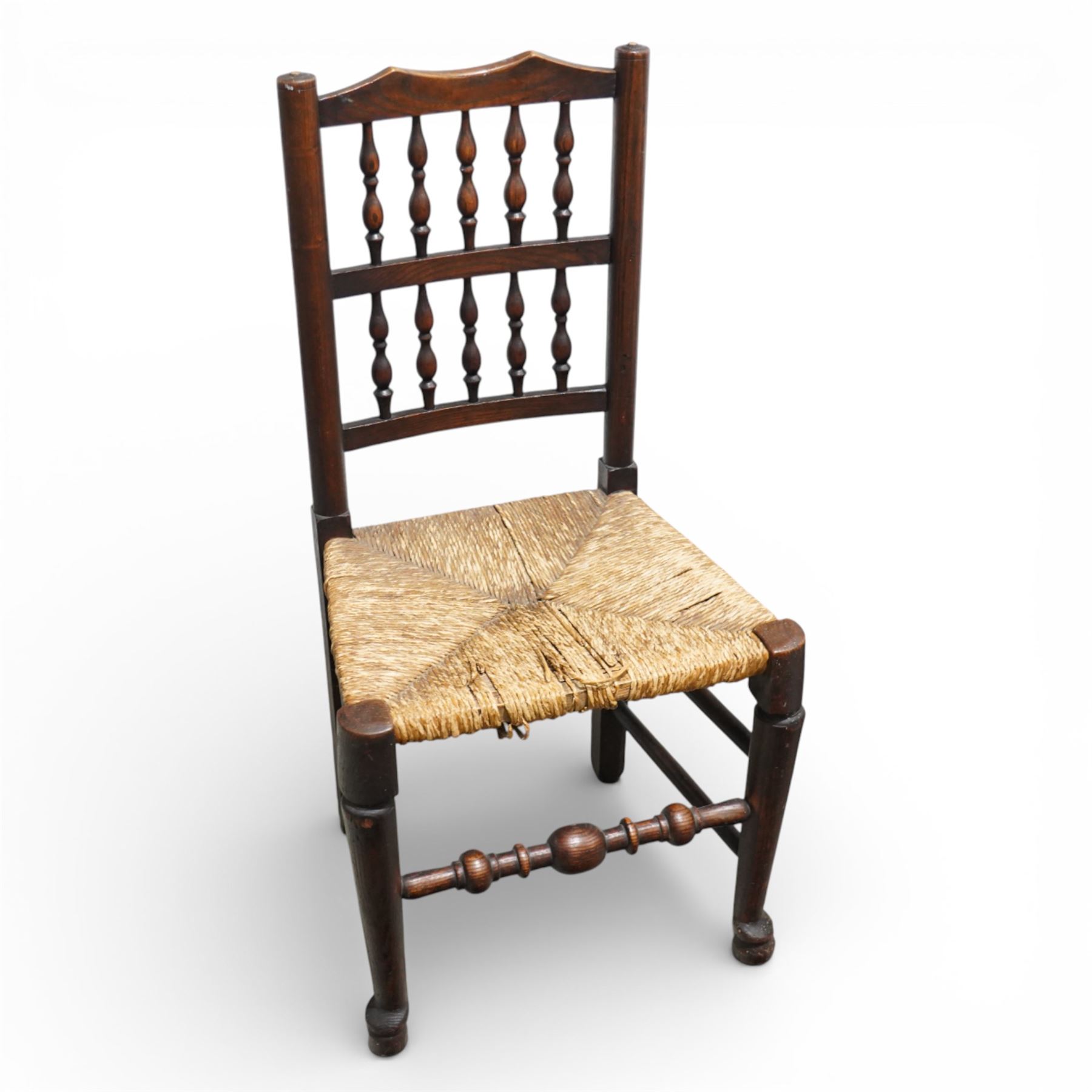 Set of five 19th century elm spindle back chairs, with shaped crest rails above double rows of turned spindles, rush seats, turned legs joined by stretchers supported on turned pad feet