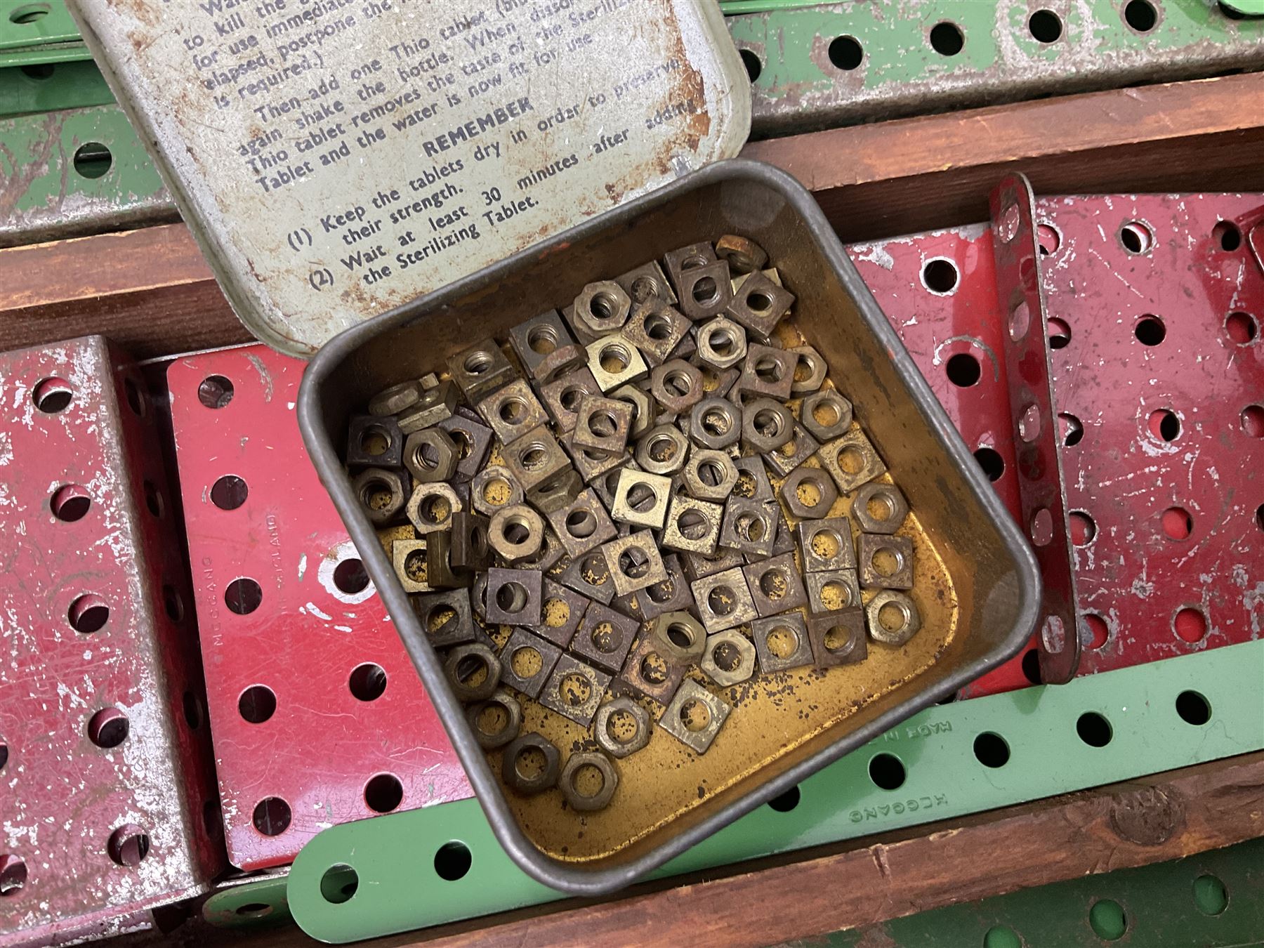 Meccano - large quantity of loose parts including various plates and strips, flanged plates, pulleys, axle rods and crank handles, wheels and tyres, gear wheels, brackets, nuts & bolts, various manuals; predominantly red and green; some in compartmentalised wooden trays