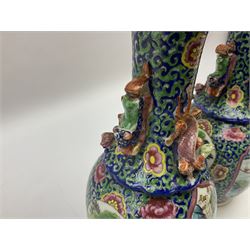 Pair of 19th Century Clobbered Chinese Export vases, with lobed rim and applied twin temple lions and dragons to the waisted neck, decorated with enamel panels of traditional scenes of figures and buildings, surrounded by blossoming flowers, H20cm