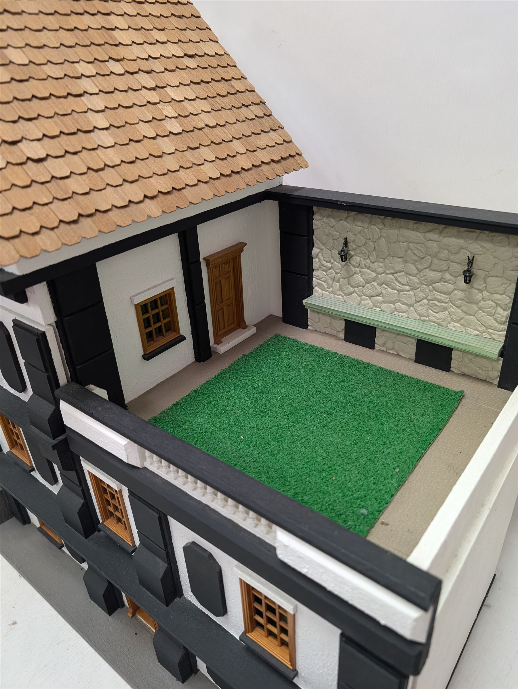 1:24 scale four-storey tudor-style dolls house, with black and white exterior, balcony garden, glazed panelled windows and wooden shingle roof, with decorated interior and wired fireplaces and lighting, H65cm, W58cm, D31cm, 