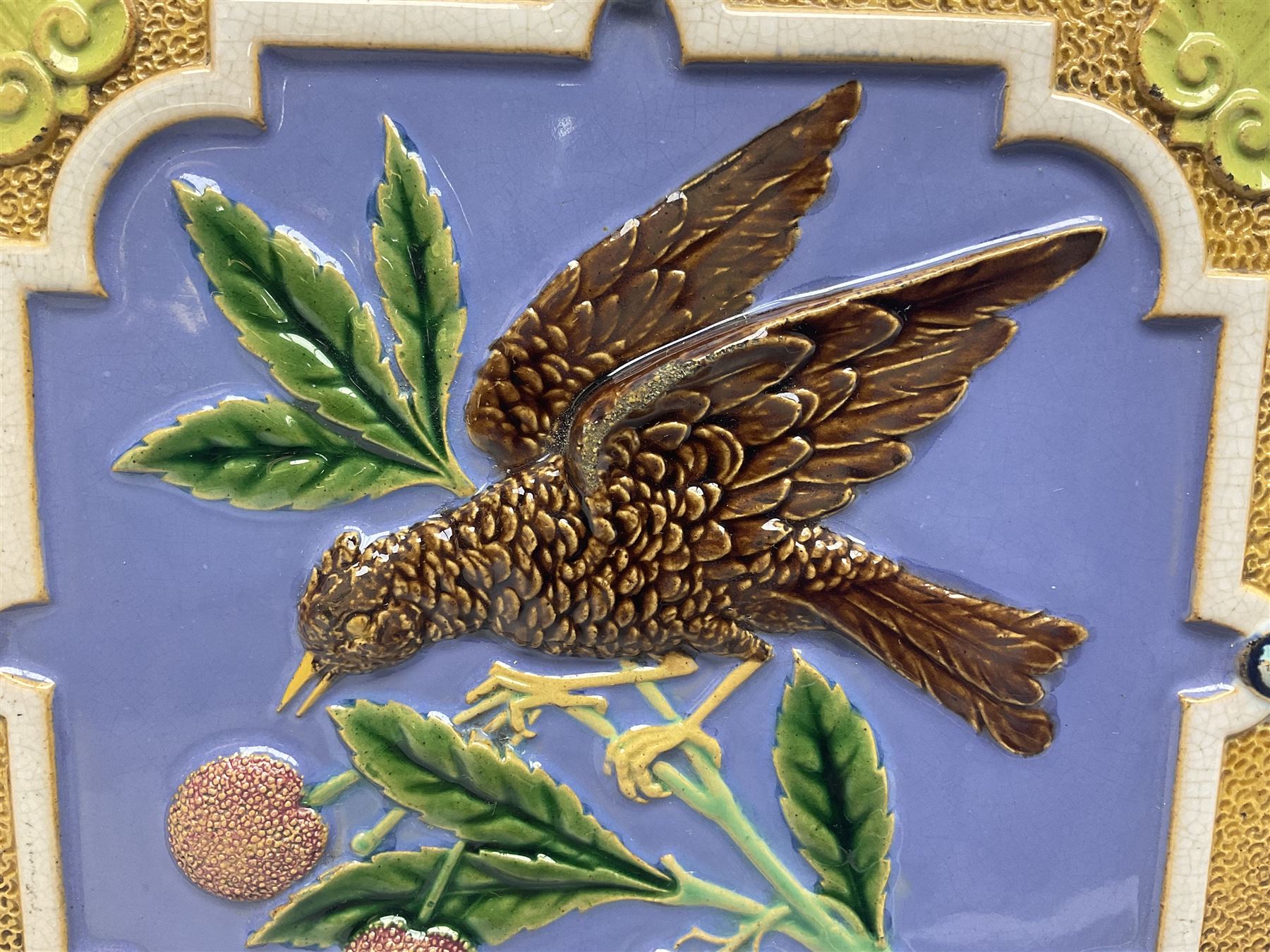 19th century Minton & Co majolica tile, decorated in relief with a bird upon a fruiting branch against a blue ground, with textured ochre border and anthemion to each corner, impressed mark verso, H19.7cm