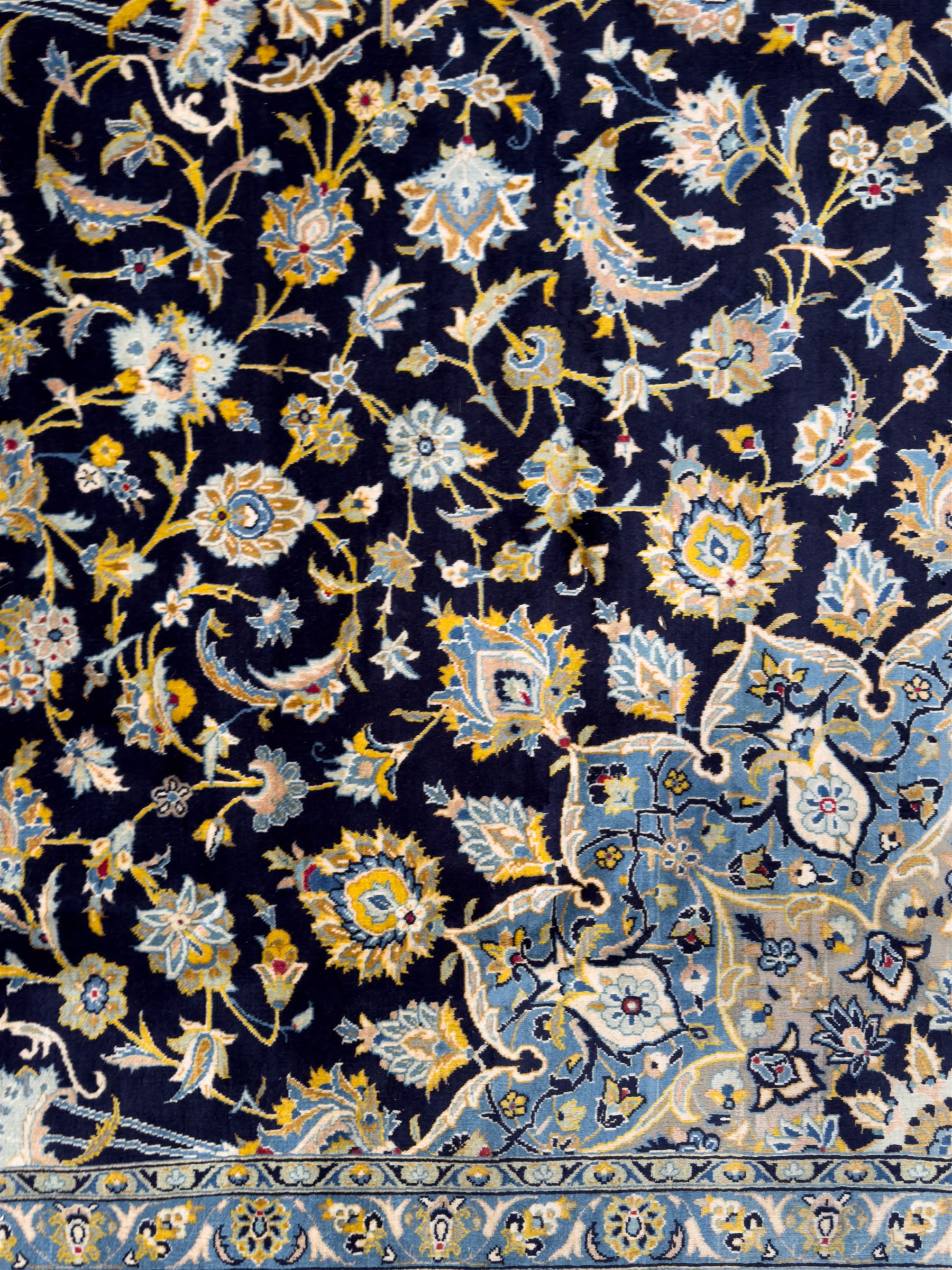 Central Persian Kashan hand-knotted carpet, the navy field with central medallion in pale blue and gold tones, surrounded by spiralling arabesques and palmettes, framed by quarter spandrels and a wide border of stylised lotus and rosette motifs between floral guard stripes, from the region of Kashan