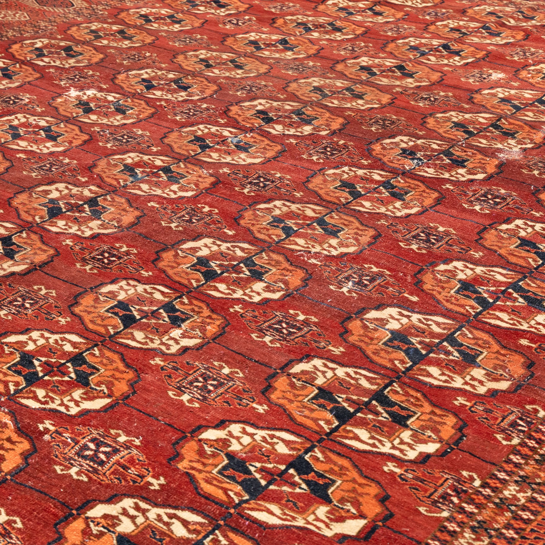 Persian Bokhara crimson ground rug, the field decorated with five rows of repeating Gul motifs with interspersed geometric design, enclosed by a guard band of further geometric-style Gul designs comprised of hook motifs