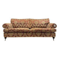 Duresta - pair of Grande three-seat sofas, traditional shaped with rolled arms and upholstered loose cushions, in red ground fabric with raised gold foliate pattern, on turned feet with brass castors 