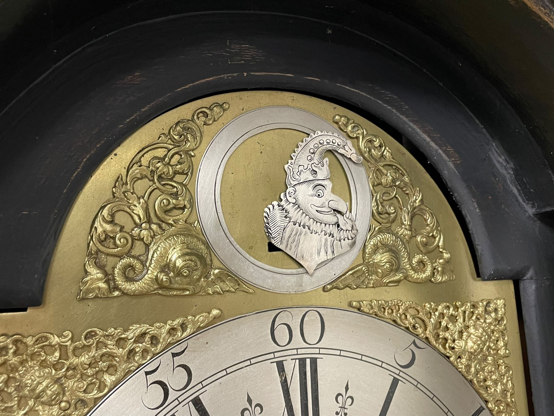 James Bowra of Sevenoaks Kent - 18th century 8-day ebonised longcase clock with gilt decoration c1740, with a flat top, dentil moulding beneath and shaped back splats, break arch hood door flanked by plain pilasters with wooden capitals, long trunk with a curved topped door, on a square plinth with canted corners and raised on a moulded base, brass dial with cast spandrels and a silvered 'Punch' automata to the arch, matted dial centre with seconds ring and date aperture, silvered chapter ring with Roman numerals, five minute Arabics, minute and quarter hour tracks, with matching steel hands and silvered makers name plate, rack striking movement with a recoil anchor escapement, striking the hours on a bell. With weights and pendulum.