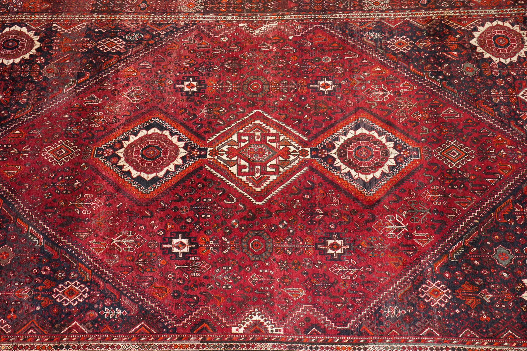 Large Persian Shiraz crimson ground carpet, the busy field decorated with a geometric pole medallion surrounded by stylised plant motifs with contrasting indigo spandrels and geometric-woven guard bands