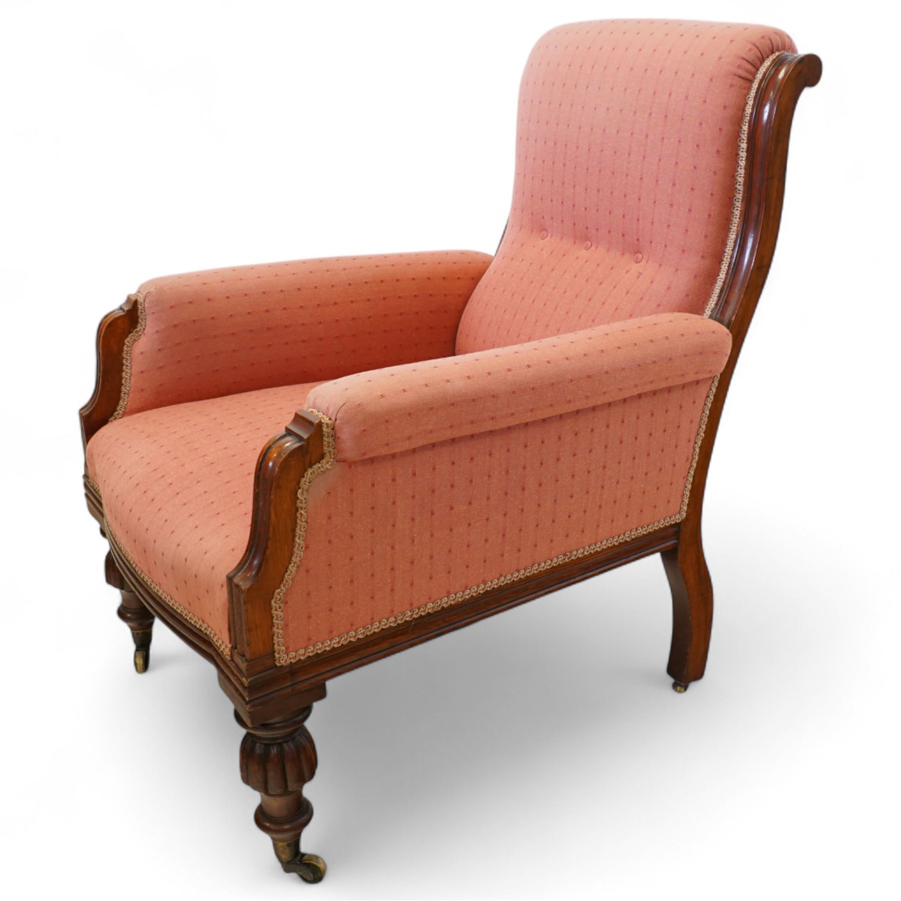 Victorian mahogany framed armchair, upholstered in salmon pink dot patterned fabric, the moulded arms with carved scroll terminals, raised on turned and fluted front legs and swept back legs, all with castors