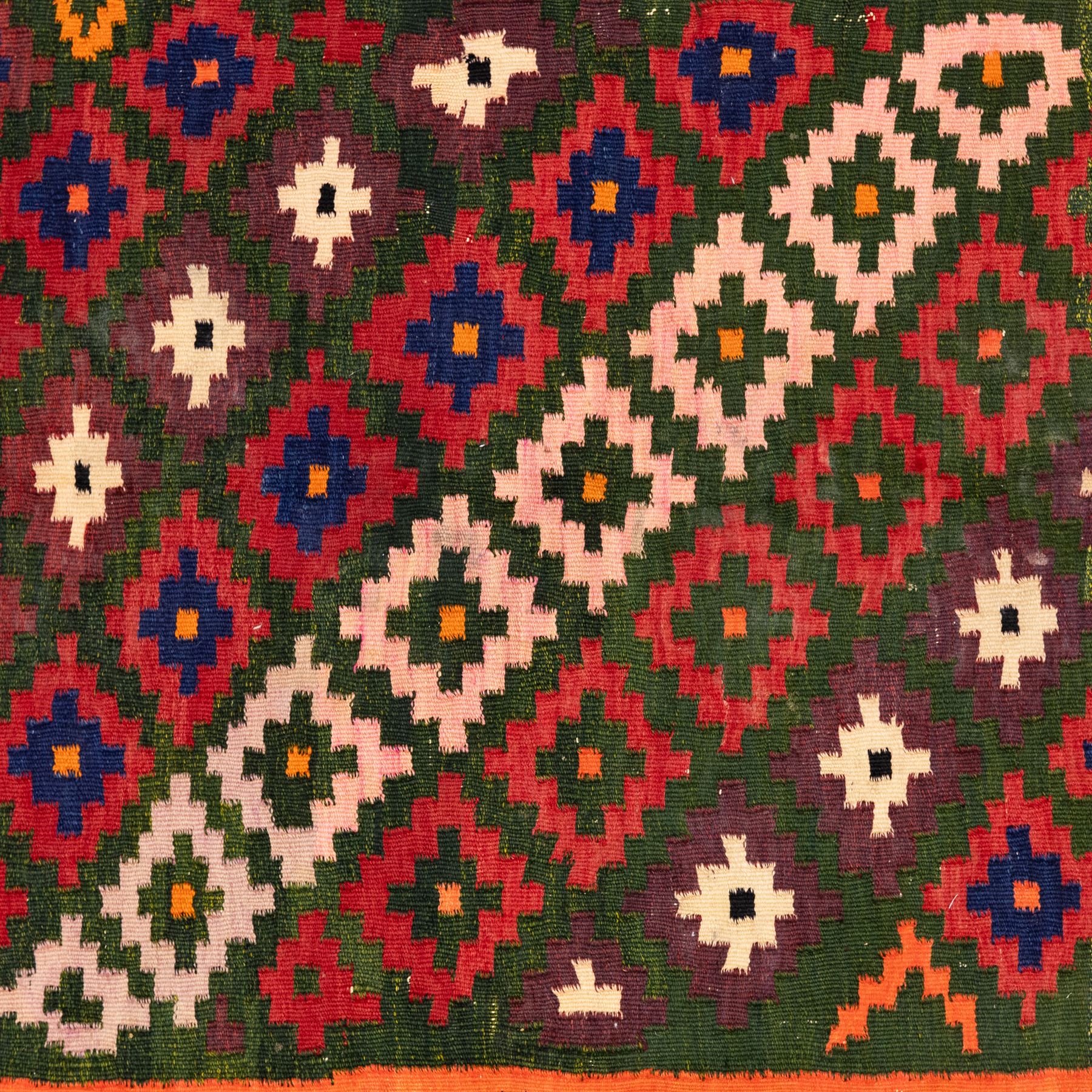 North East Persian Sumak flatweave kilim, woven with an all-over arrangement of stepped diamond motifs, including a diagonal band of contrasting colours in shades of red, indigo, green, pink, and ivory, framed by multiple geometric borders incorporating serrated chevron designs  