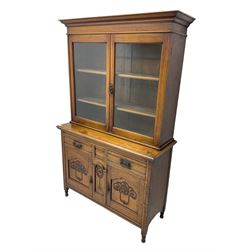 Edwardian walnut bookcase cabinet on cupboard, fitted with two glazed doors above two drawers and two cupboards, the lower cupboard enclosed by two doors carved with tulip motifs