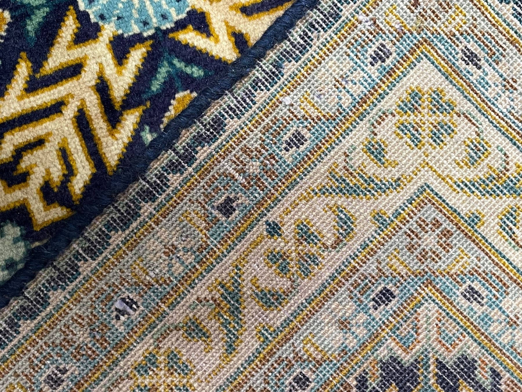 Persian indigo and pale gold ground rug, overall busy geometric design, the field decorated with hooked Hac and palmette medallions surrounded by densely patterned zig-zags and stylised foliate motifs, the border decorated with smaller Hac motifs, within multiple guard stripes 