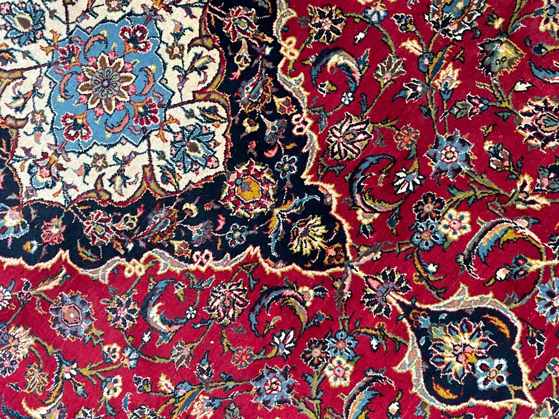 Persian Kashan crimson ground carpet, the central pole medallion decorated with flower heads, surrounded by trailing leafy branches and palmettes, scrolling border decorated with further palmettes, within floral pattern guard stripes 